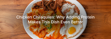 Plate of chicken chilaquiles topped with red salsa, melted cheese, and green onions, served with shredded beef, refried beans, queso fresco, and two sunny-side-up eggs on a wooden table.