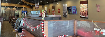 Interior of Loaded Cafe with front counter, glass display case, holiday garland decor, dining tables, and wall art with digital menu screens.