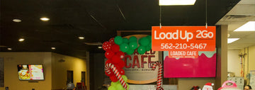 Loaded Cafe interior with a “Load Up 2Go” takeout sign and phone number 562-210-5467 hanging above festive red and green balloons.