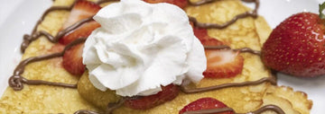 Strawberry crepes topped with whipped cream and drizzled with chocolate, served on a white plate with fresh strawberries.