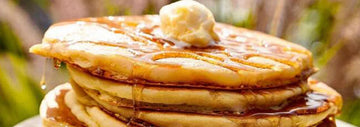 Stack of fluffy pancakes topped with butter and drizzled with maple syrup.