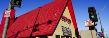 Loaded Cafe exterior with bright red roof, roadside sign, and traffic lights at a street intersection under a clear blue sky.