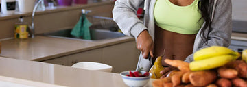 Person in a kitchen slicing a pear beside a bowl of berries, with bananas and sweet potatoes on the counter in the foreground.